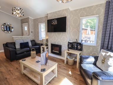 A living room with two black leather sofas a wooden coffee table a wall-mounted television a stereo system and windows with blinds at Ghyll Lodge Grasmere 25 White Cross Bay Windermere