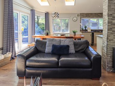 A black leather sofa with three cushions in front of a wooden dining table and kitchen at Ghyll Lodge Grasmere 25 White Cross Bay Windermere