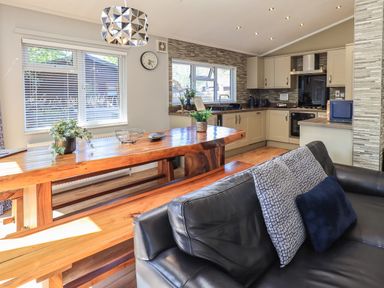 A kitchen and dining area with wooden table and bench a black leather sofa and plants at Ghyll Lodge Grasmere 25 White Cross Bay Windermere