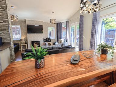 A living room with leather sofas a wall mounted television and a wooden table with plants at Ghyll Lodge Grasmere 25 White Cross Bay Windermere