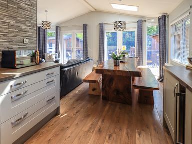 A dining area with a wooden table and benches and a black leather sofa near large windows at Ghyll Lodge Grasmere 25 White Cross Bay Windermere