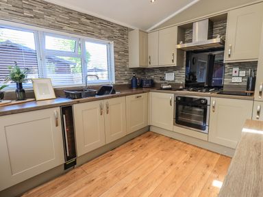 A kitchen with cabinets a sink an oven a stove a range hood and a window with blinds at Ghyll Lodge Grasmere 25 White Cross Bay Windermere