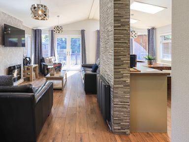A living room with black leather sofas a coffee table a wall mounted television and glass doors leading outside at Ghyll Lodge Grasmere 25 White Cross Bay Windermere