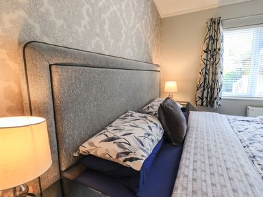A bedroom with a bed with patterned pillows and cushions bedside tables with lamps and a window with blinds and patterned curtains at Ghyll Lodge Grasmere 25 White Cross Bay Windermere