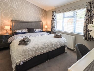 A bedroom with a bed folded towels bedside tables and lamps next to a window with blinds and curtains at Ghyll Lodge Grasmere 25 White Cross Bay Windermere