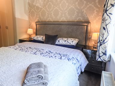 A bedroom with a bed with patterned bedding and towels on it two bedside tables with lamps and a window with curtains at Ghyll Lodge Grasmere 25 White Cross Bay Windermere