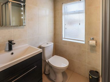A bathroom with a toilet sink with black faucet mirror window with blinds toilet paper holder and small trash bin at Ghyll Lodge Grasmere 25 White Cross Bay Windermere