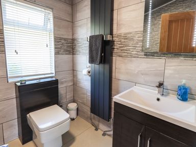 A bathroom with a toilet under a window a sink with a mirror above and a towel hanging on a vertical radiator at Ghyll Lodge in Grasmere 25 White Cross Bay Windermere