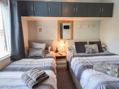 A bedroom with two beds each with folded towels a bedside table with a lamp and a mirror above at Ghyll Lodge Grasmere 25 White Cross Bay Windermere