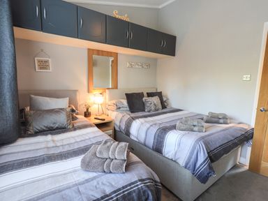 A bedroom with two beds striped bedding folded towels and wall cabinets at Ghyll Lodge Grasmere 25 White Cross Bay Windermere