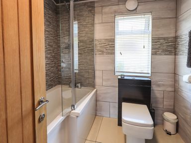A bathroom with a bathtub shower combination a toilet a small window with blinds and a wooden door at Ghyll Lodge Grasmere 25 White Cross Bay Windermere