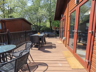 A wooden deck with outdoor dining tables, chairs, and a sofa next to a wooden building at Ghyll Lodge Grasmere 25 White Cross Bay Windermere