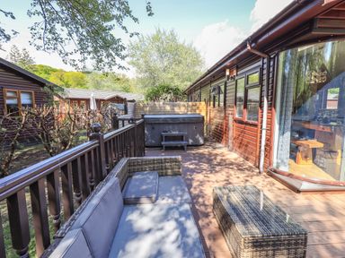 A wooden deck with outdoor seating and a hot tub next to a wooden lodge at Ghyll Lodge Grasmere 25 White Cross Bay Windermere