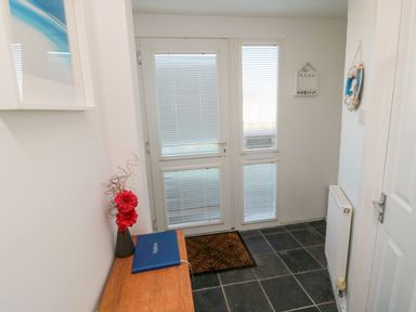 An entryway with a wooden table with a vase and a blue book a door with blinds and a black tiled floor at Barnacles in Boulmer near Longhoughton