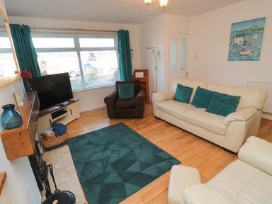A living room with cream sofas blue cushions a brown armchair a turquoise rug a television and a painting at Barnacles Boulmer near Longhoughton