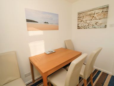 A dining area with a wooden table and four cream chairs with beach-themed wall art at Barnacles in Boulmer near Longhoughton