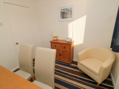 A small dining area with two cream chairs a wooden sideboard with a lamp and radio and a cream armchair at Barnacles in Boulmer near Longhoughton