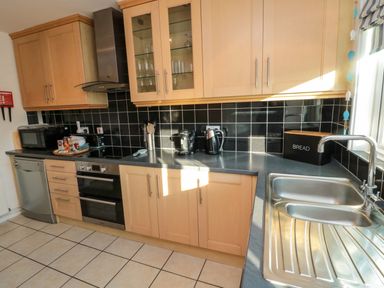 A kitchen with wooden cabinets black tiled backsplash a double sink dishwasher oven microwave toaster kettle and a bread box at Barnacles Boulmer near Longhoughton