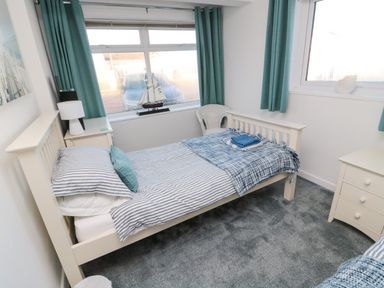 A single bed with striped bedding and a blue blanket in a bedroom with teal curtains and white furniture at Barnacles Boulmer near Longhoughton