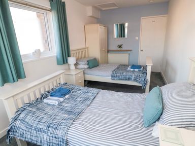 A bedroom with two single beds nightstand wardrobe and window with teal curtains at Barnacles Boulmer near Longhoughton