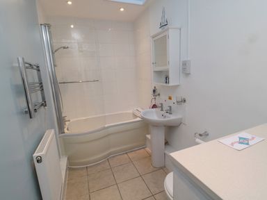 A bathroom with a bathtub shower combination white sink mirror cabinet and tiled floor at Barnacles in Boulmer near Longhoughton