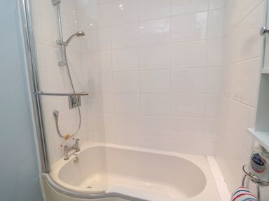 A bathroom with a bathtub shower combination and white tiled walls at Barnacles Boulmer near Longhoughton