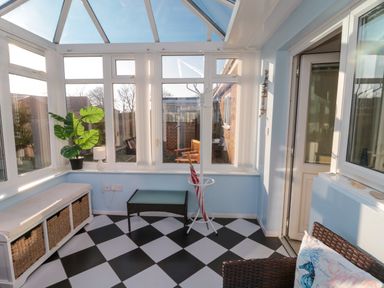 A conservatory with black and white checkered floor a bench with baskets a potted plant a small table and a coat rack at Barnacles in Boulmer near Longhoughton