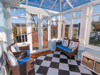 A conservatory with wicker chairs with cushions and a storage bench at Barnacles in Boulmer near Longhoughton