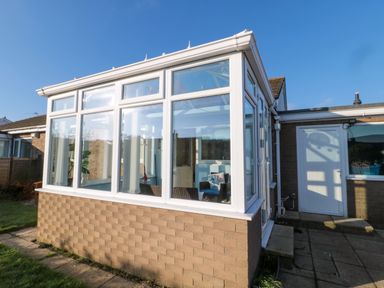 An exterior view of a conservatory with white framed windows attached to a brick house at Barnacles in Boulmer near Longhoughton