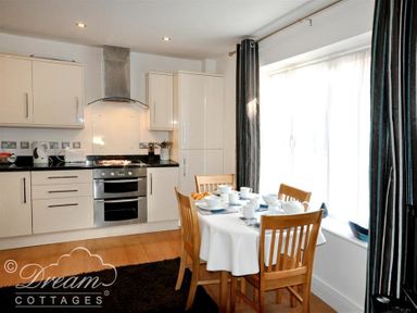A kitchen with white cabinets a stove and a dining table with chairs set for a meal at Admirals Quarter Apartment 5 in Weymouth