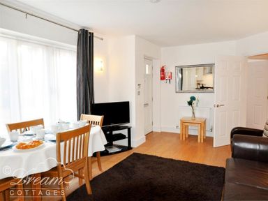 A dining area with a table set for tea next to a living area with a television and brown sofa at Admirals Quarter Apartment 5 in Weymouth