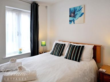A bedroom with a double bed two striped pillows bedside tables lamps and a window with curtains at Admirals Quarter Apartment 5 in Weymouth