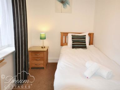 A bedroom with a single bed, bedside table with a lamp, and window with striped curtains at Admirals Quarter Apartment 5 in Weymouth
