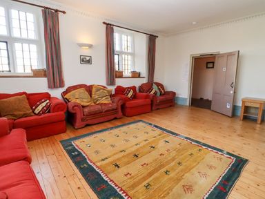 A living room with multiple red armchairs and a large patterned rug on a wooden floor at Wick Court Farm in Arlingham near Frampton On Severn