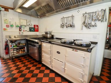 A commercial kitchen with a large white stove utensils hanging on the wall and shelves with spices at Wick Court Farm in Arlingham near Frampton On Severn