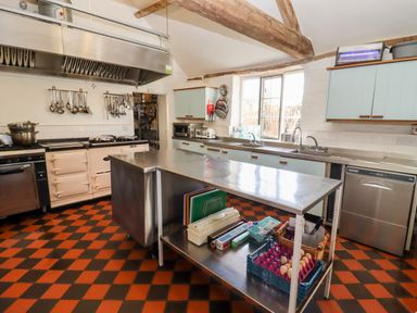 A kitchen with stainless steel work tables an oven a dishwasher hanging utensils and a window at Wick Court Farm in Arlingham near Frampton On Severn