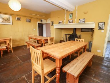A dining room with wooden tables benches and chairs a fireplace and framed pictures on yellow walls at Wick Court Farm in Arlingham near Frampton On Severn