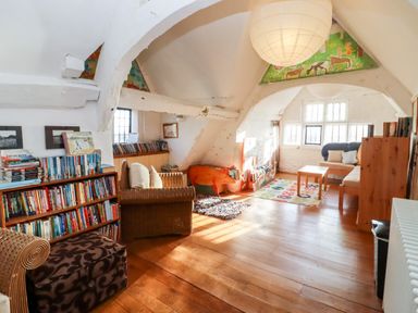 A loft room with bookshelves, wicker chairs, a sofa, a wooden coffee table, and a colorful rug at Wick Court Farm Arlingham near Frampton On Severn
