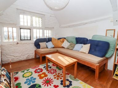 A sitting room with a wooden sofa, colorful cushions, a wooden table, a floral rug, and windows at Wick Court Farm in Arlingham near Frampton On Severn
