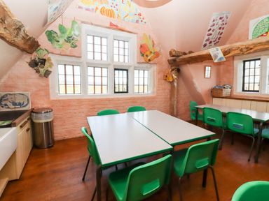A classroom with green chairs and tables near windows with educational posters on peach walls at Wick Court Farm in Arlingham near Frampton On Severn