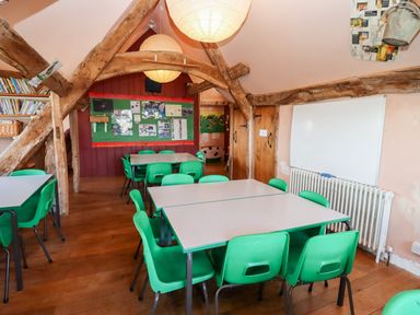 A classroom with green chairs and white tables wooden beams on the ceiling and a whiteboard on the wall at Wick Court Farm Arlingham near Frampton On Severn