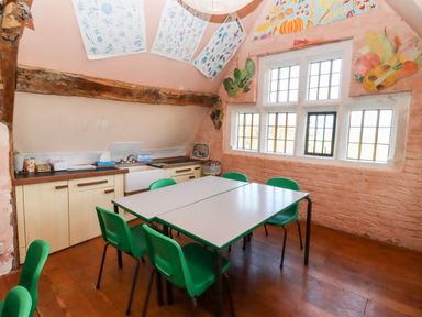 A small kitchen or classroom with a table and green chairs under slanted ceiling with botanical posters at Wick Court Farm Arlingham near Frampton On Severn