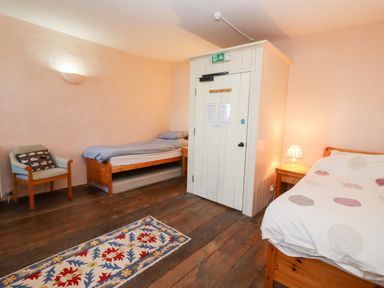 A bedroom with two wooden beds a chair a wooden floor and a patterned rug at Wick Court Farm Arlingham near Frampton On Severn