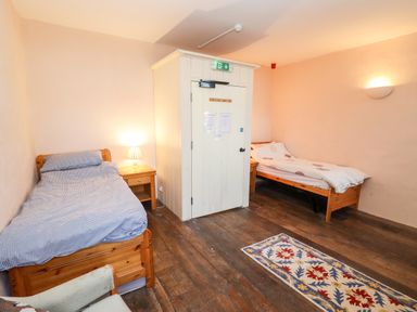 A bedroom with two single beds a wooden floor a small rug and a white enclosed structure at Wick Court Farm in Arlingham near Frampton On Severn