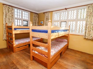 A bedroom with two wooden bunk beds and windows with floral curtains at Wick Court Farm in Arlingham near Frampton On Severn