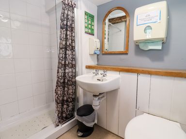 A bathroom with a shower, sink, mirror, trash can, and paper towel dispenser at Wick Court Farm Arlingham near Frampton On Severn