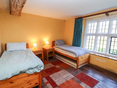 A bedroom with two single beds two bedside tables with lamps a large window and a patterned rug at Wick Court Farm Arlingham near Frampton On Severn