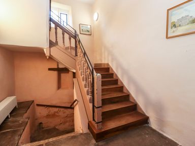 A staircase with wooden steps and handrails in a hallway with peach and white walls and framed pictures at Wick Court Farm in Arlingham near Frampton On Severn