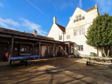 An outdoor courtyard with a ping pong table benches a tree and a building with windows at Wick Court Farm Arlingham near Frampton On Severn