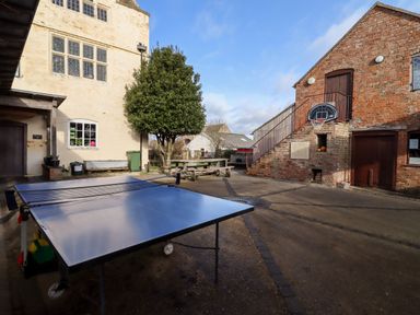 An outdoor courtyard with a ping pong table a basketball hoop on a brick building and a tree near a picnic table at Wick Court Farm Arlingham near Frampton On Severn